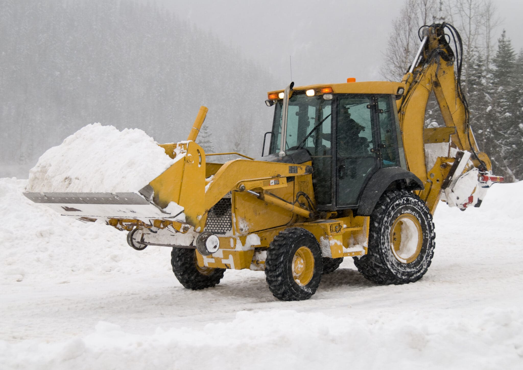 Front End Loader Clearing Snow Yellow backhoe loader moving snow in winter.