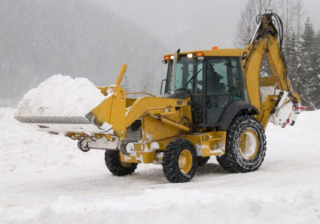Yellow backhoe loader moving snow in winter.